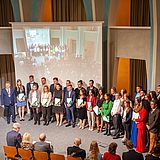 Personen mit Urkunden in der Hand nebeneinander vor einem Projektionsschirm